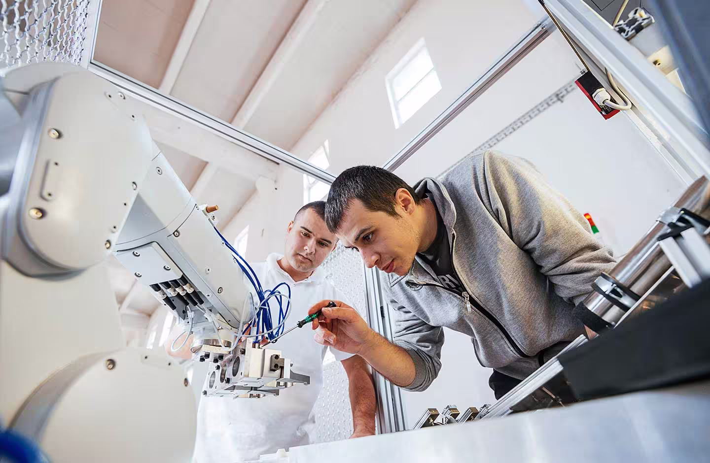 Two Wes-Tech engineers work on a white robotic arm.
